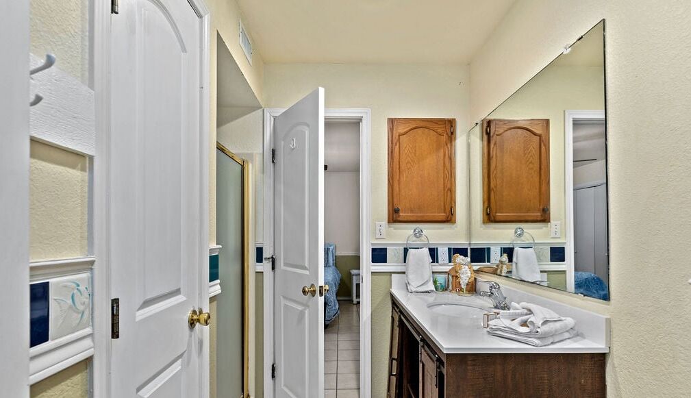 A bathroom with two sinks, wooden cabinets, a large mirror, and a door leading to another room.