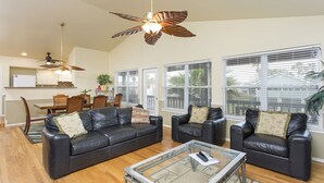 A spacious living room with two black leather sofas, a glass coffee table, and a ceiling fan with leaf-shaped blades. - Bahama Beach House • Private Heated Pool & Hot Tub • 3 Min Walk to Beach (South Padre Island)