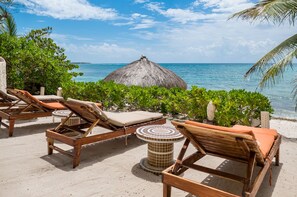 A beachside lounge area with wooden lounge chairs and a thatched umbrella, overlooking the ocean.