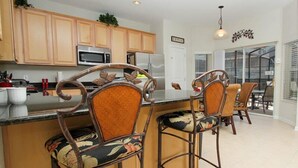 A kitchen with wooden cabinets, a microwave, and a refrigerator. There are two bar stools with floral upholstery. - 6 Bed/4 Bath Villa POOL FACES SOUTH!  2 Miles From DISNEY 130 Reviews 9.8 rating (Kissimmee)