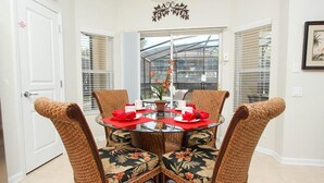 A dining area with a round glass table, four wicker chairs with floral upholstery, and a ceiling light fixture. - 6 Bed/4 Bath Villa POOL FACES SOUTH!  2 Miles From DISNEY 130 Reviews 9.8 rating (Kissimmee)