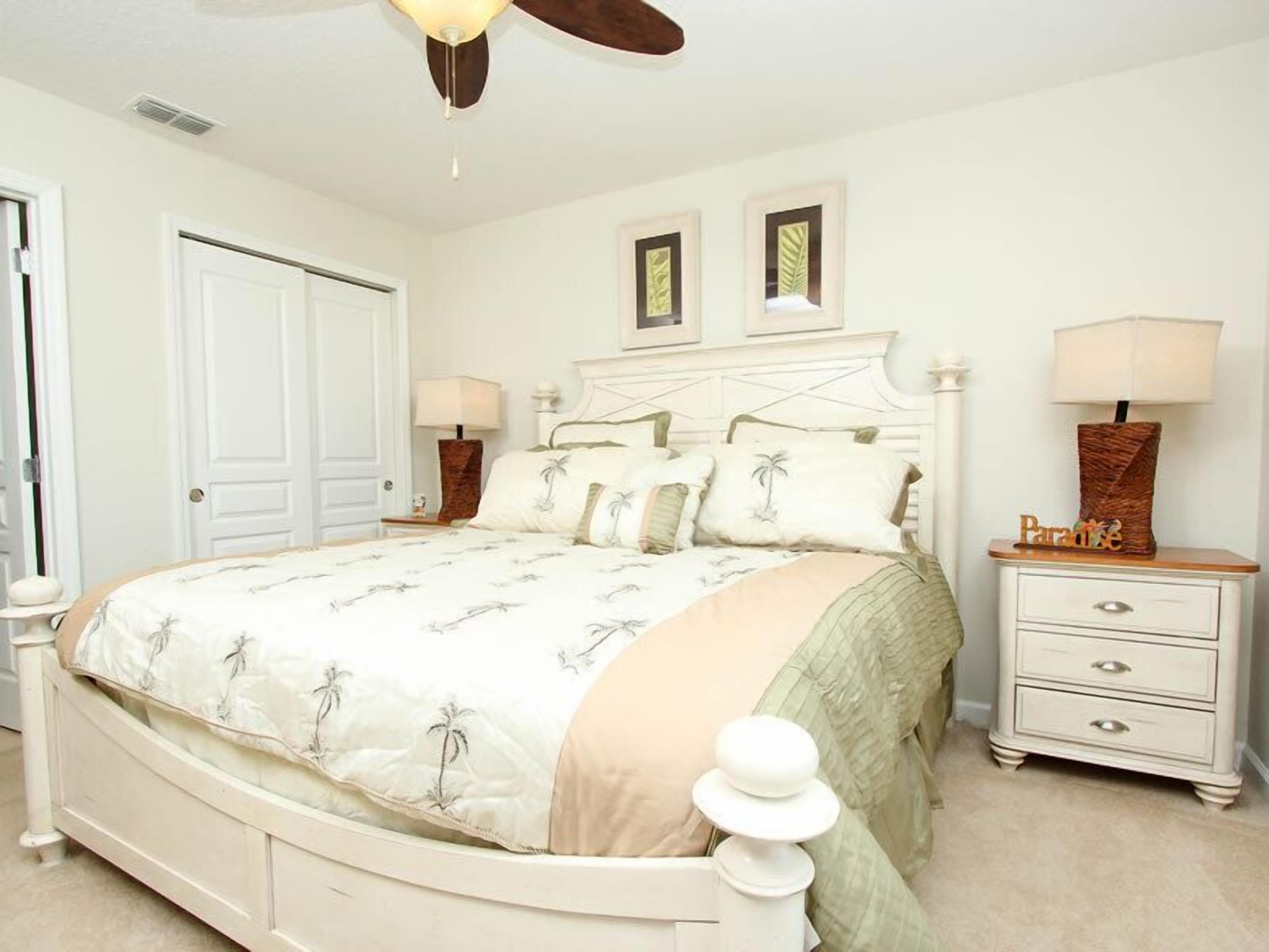 Une chambre à coucher comprenant un lit, deux tables de chevet, une commode, un ventilateur de plafond et une porte.