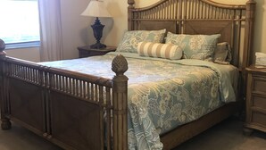 Une chambre à coucher avec un lit en bois, une table de chevet, une lampe et une fenêtre avec des rideaux.
