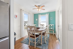 A dining area with a round table, white chairs, a ceiling fan, and a view through the window. - "Holden You" - Oceanfront Home w/ Pool, 5 Bedrooms / 3 Bathrooms (Holden Beach)