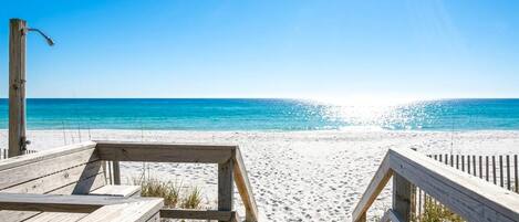 A wooden boardwalk leading to a sandy beach with clear blue water.