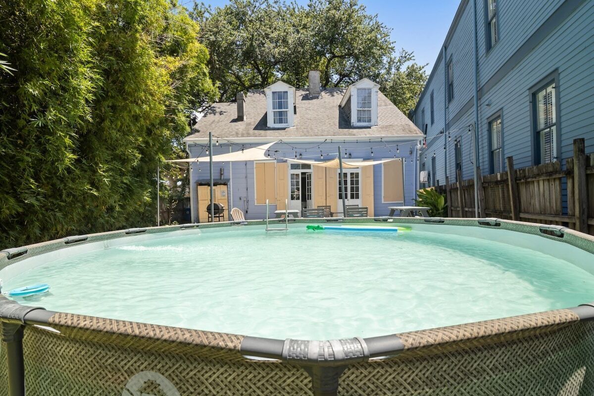 A swimming pool with a covered patio area and a house in the background.