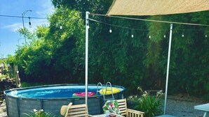 An outdoor patio with a pool, wooden chairs, a picnic table, and a patterned rug.