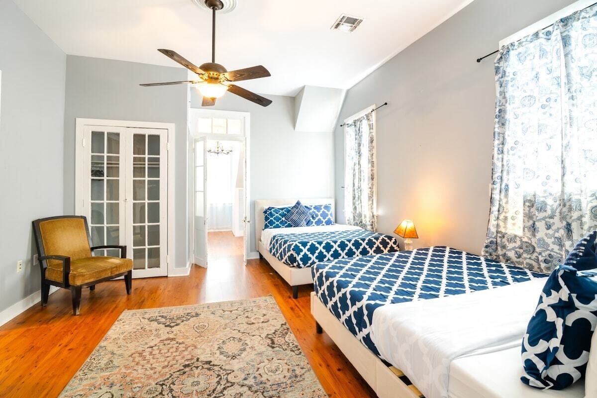 A bedroom with two beds, a ceiling fan, a chair, and a door leading to a hallway.