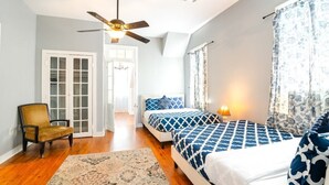 A bedroom with two beds, a ceiling fan, a chair, and a door leading to a hallway.