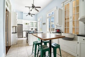 A kitchen with white cabinets, a wooden table, green stools, and ceiling fans. - Historic Governor's Home w/ Pool, Near French Quarter (New Orleans)