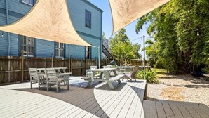 A wooden deck with picnic tables and chairs, a blue building in the background, and a bamboo fence.