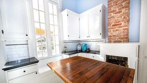 A kitchen with white cabinets, a wooden table, and a brick wall.