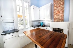 A kitchen with white cabinets, a wooden table, and a brick wall. - Historic Governor's Home w/ Pool, Near French Quarter (New Orleans)