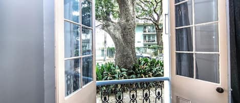 A door with a view of a tree and a balcony with a metal railing.