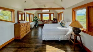 A spacious bedroom with a large bed, wooden dresser, and a desk with a chair. There are multiple windows providing views of the outdoors. - Teton View - Cache Vista Ranch Estate - Sleeps 32 (Tetonia)