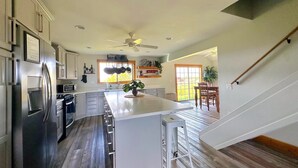 A modern kitchen with a large island, stainless steel appliances, and a dining area with a view. - Teton View - Cache Vista Ranch Estate - Sleeps 32 (Tetonia)