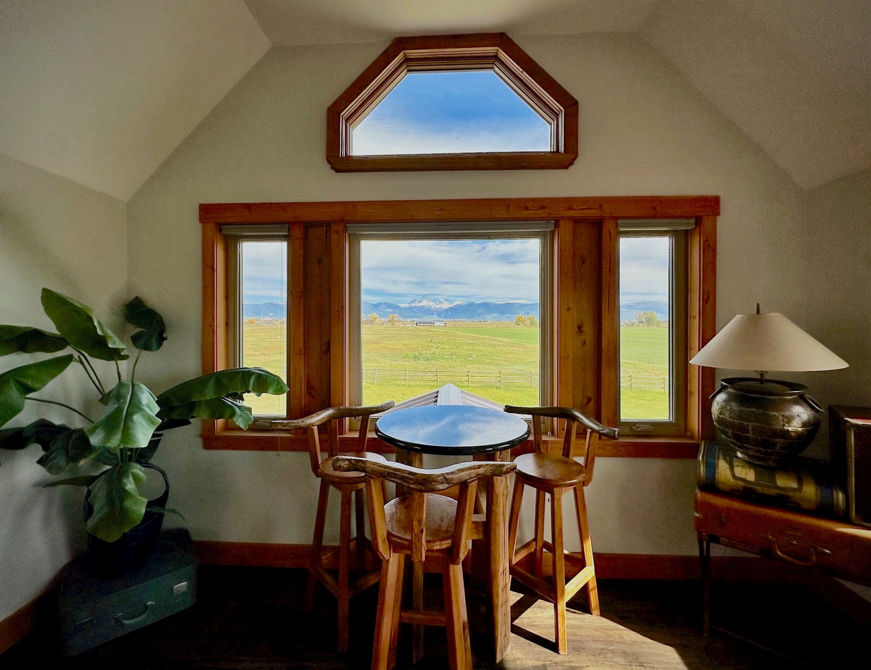 A room with a table and chairs facing a large window with a view of mountains.