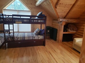 Cozy cabin-style room with a bunk bed, wooden flooring, and sloped ceiling with exposed beams.