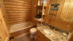Un baño de cabaña de madera con bañera, inodoro, lavamanos de encimera de granito y armarios de madera.