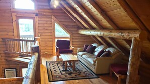 Acogedor dormitorio en el ático con techo de madera, un sofá, una mesa y vistas a través de una ventana.