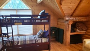 Una cama litera con ventana, una silla verde y un estante de madera con objetos.