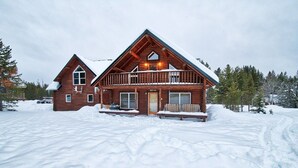 En stuga av trä med en balkong, omgiven av snö.