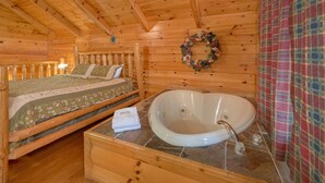 A wooden cabin bedroom with a bed, a large bathtub, and a decorative wreath on the wall. - Affordable Hot tub cabin | Cozy | Quiet (Pigeon Forge)