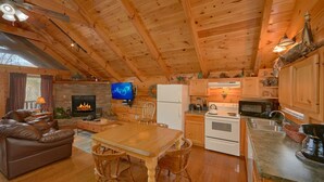 A cozy cabin interior with a fireplace, wooden ceiling, a dining area, and a kitchen with basic appliances. - Affordable Hot tub cabin | Cozy | Quiet (Pigeon Forge)