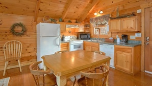 A wooden cabin kitchen with a dining table and chairs, a refrigerator, microwave, stove, and dishwasher. - Affordable Hot tub cabin | Cozy | Quiet (Pigeon Forge)