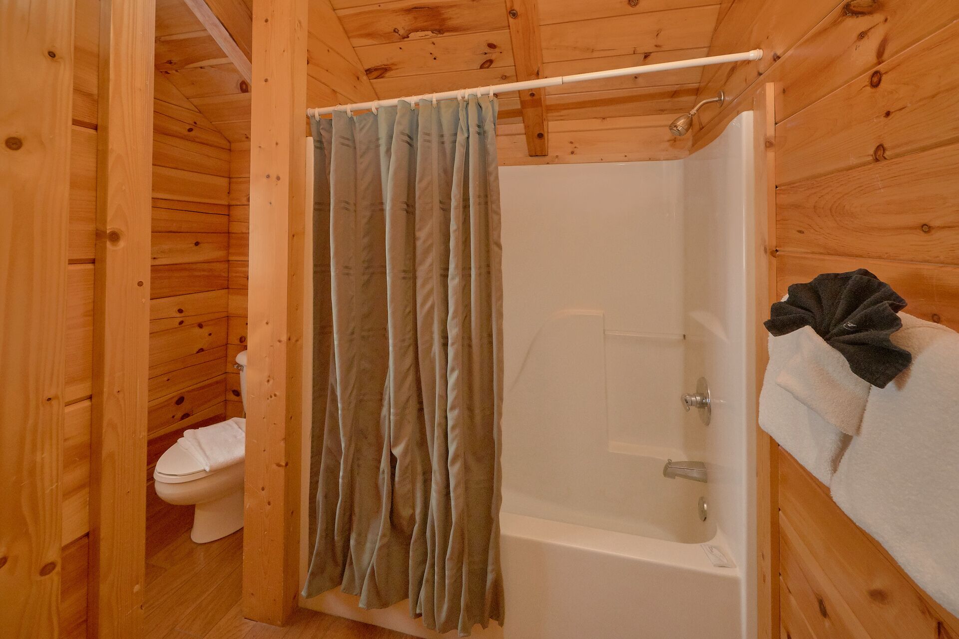 A wooden cabin bathroom with a shower curtain, a toilet, and a bathtub.