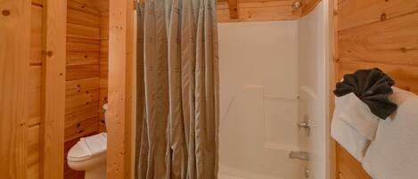 A wooden cabin bathroom with a shower curtain, a toilet, and a bathtub.