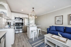 Een moderne keuken met roestvrijstalen apparatuur, een centraal eiland en een blauwe bank in de woonkamer.