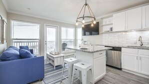 A modern kitchen with white cabinets, a stainless steel dishwasher, and a central island with bar stools. - Trendy Beach Condo- Sunset views, Sandy Toes, Surfing more... (1304) (Galveston)