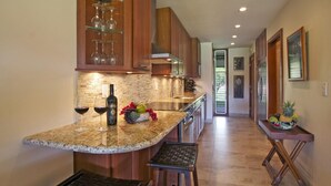 Una cocina con encimeras de granito, armarios de madera, un lavamanos de acero inoxidable y una pequeña isla con taburetes.