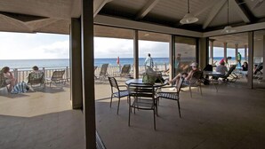 Un área de estar al aire libre con mesas y sillas frente a la playa.
