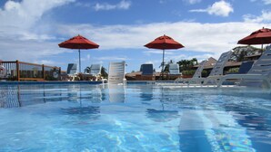 Una piscina cristalina con sillones de descanso y sombrillas rojas.