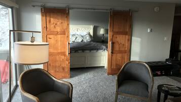 A bedroom with a bed, a nightstand, a lamp, and two chairs.