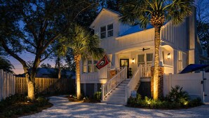 A two-story house with a front porch, a flag, and a staircase leading to the entrance. - Indigo Cottage: Stylish Island Retreat | Walkable to Everything | Pool + Spa | Dogs Welcome (Saint Simons Island)