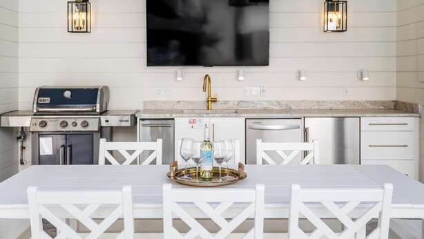 A modern kitchen with a flat-screen TV, built-in grill, and white cabinetry. - Indigo Cottage: Stylish Island Retreat | Walkable to Everything | Pool + Spa | Dogs Welcome (Saint Simons Island)