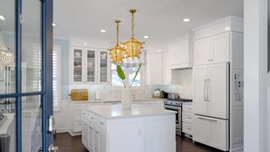 A spacious kitchen with white cabinetry, a large island, and modern appliances. - Indigo Cottage: Stylish Island Retreat | Walkable to Everything | Pool + Spa | Dogs Welcome (Saint Simons Island)