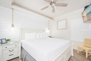 A bedroom with a large bed, a nightstand, a chair, a ceiling fan, and a wall-mounted TV. - PREMIUM One Bedroom at Phoenix V! (Orange Beach)