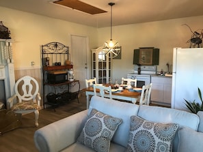 A living room with a sofa, dining table, and chairs. There is a kitchen area with a refrigerator, stove, and cabinets. A chandelier hangs from the ceiling. - Private Cozy Studio in Navarre FL (Navarre)