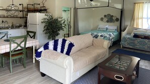 A cozy living room with a sofa, a coffee table, a dining table with chairs, a kitchen area, and a bed with a canopy.
