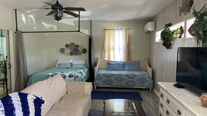 A compact living room with a sofa, two beds, a TV, and a ceiling fan.