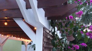 A patio area with a pergola, outdoor seating, and flowering plants.