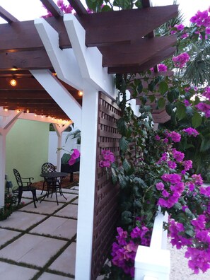 A patio area with a pergola, outdoor seating, and flowering plants.