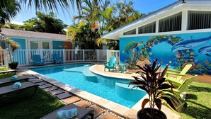 A swimming pool with a mural of marine life, surrounded by a white fence and lounge chairs.