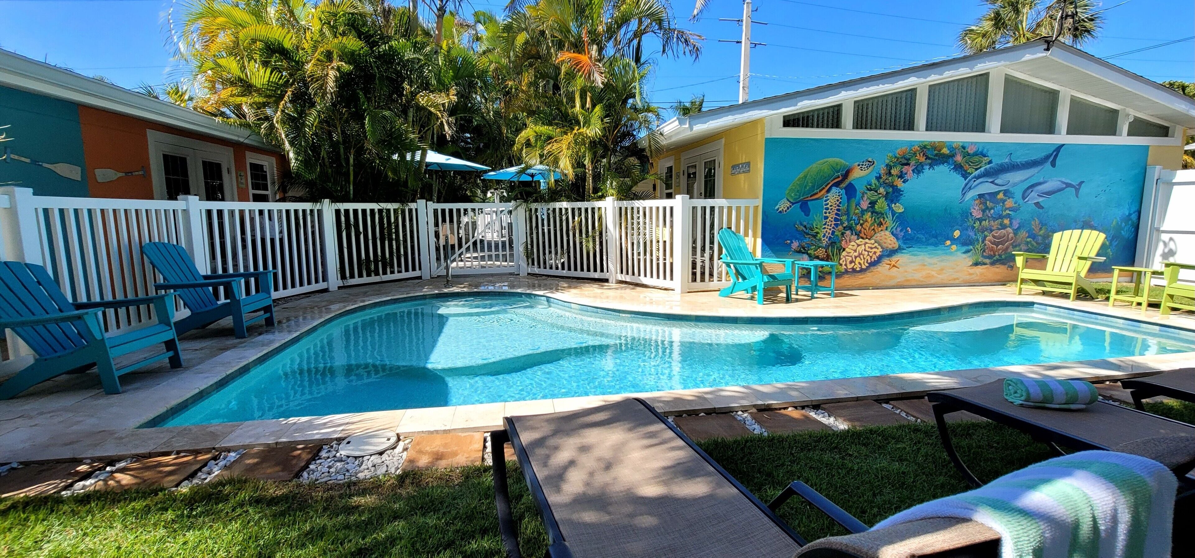 A swimming pool with blue chairs, a mural of sea creatures, and a fenced yard.
