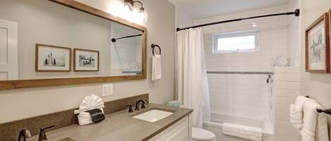 Une salle de bain avec deux lavabos, des toilettes, une douche avec une porte en verre et un grand miroir agrémenté de luminaires fixés au mur.