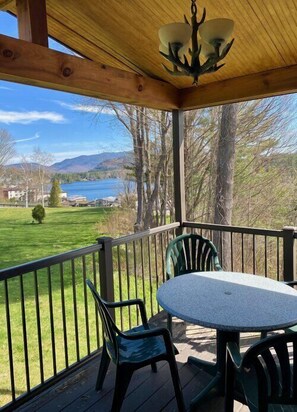 A covered outdoor area with a table and chairs, overlooking a lake and mountains. - Grand View Cottage 3 Bedroom (Lake Placid)
